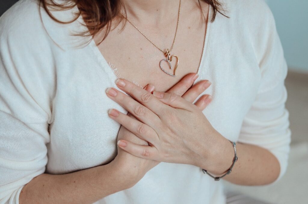 Die Hände einer Frau auf dem Herzen während der Meditation. Biohacking-, Yoga-, Entspannungs- und Meditationskonzept. Herzförmiger Anhänger am Hals des Mädchens.