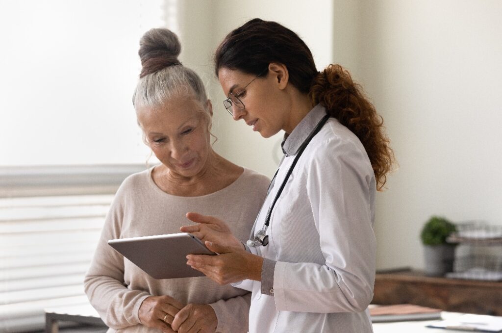 Seriöser Hausarzt zeigt einer alten Patientin den Tablet-Bildschirm